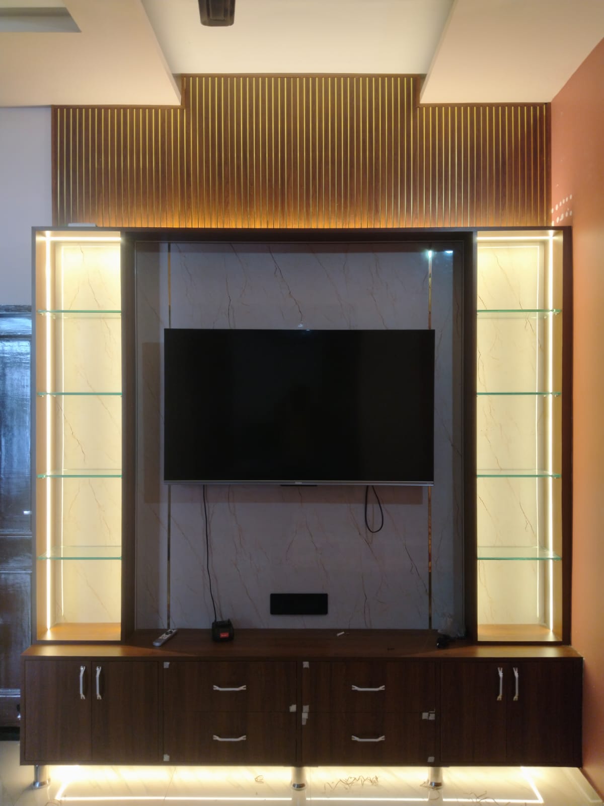 The same wall at night with the LED cove lighting on, the marble panel and glass shelves glowing